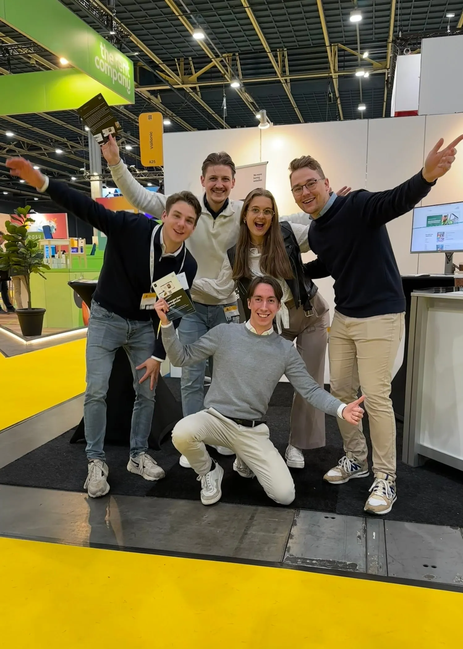 Five of the team at the Vallonic stand at a trade fair, arms in the air and cheering.