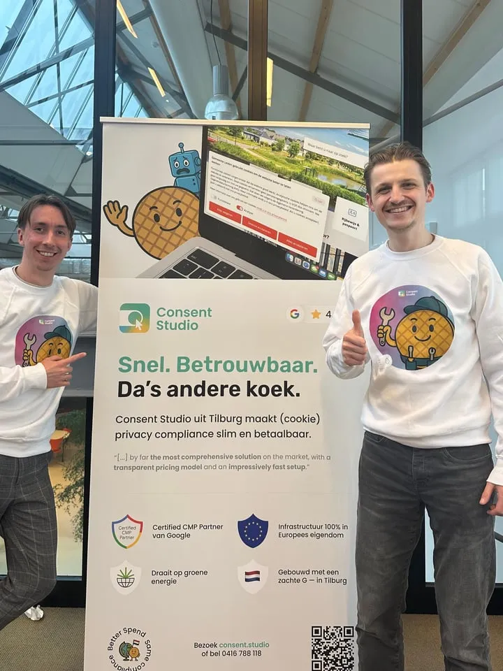 Two of the team in Consent Studio sweaters, standing either side of a Consent Studio banner at an event.